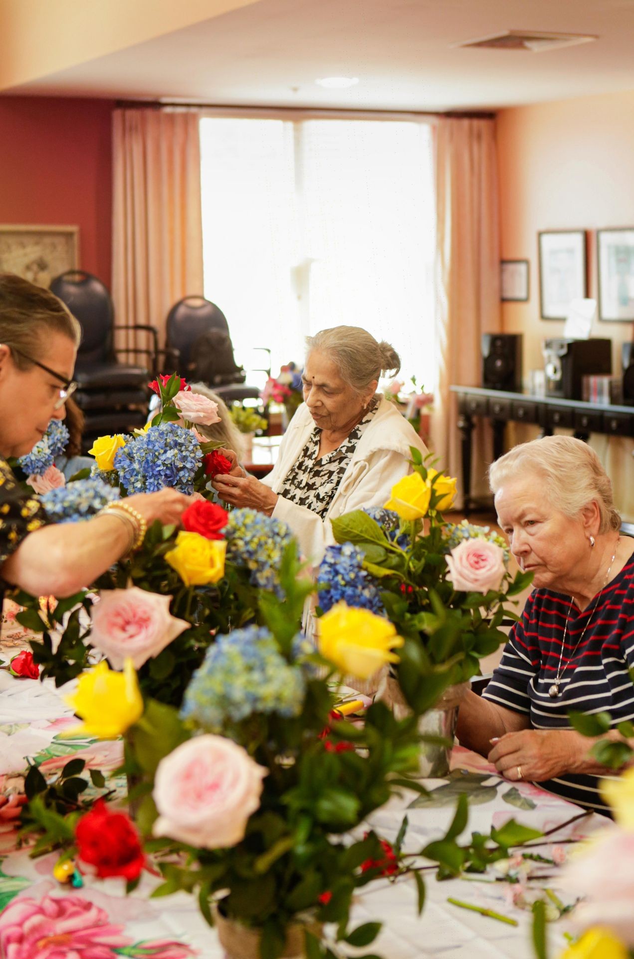 Three elderly women arranging colorful flowers in a warmly lit room.